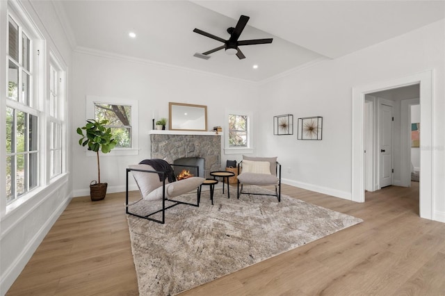 living area featuring a stone fireplace, visible vents, light wood-style floors, and ornamental molding