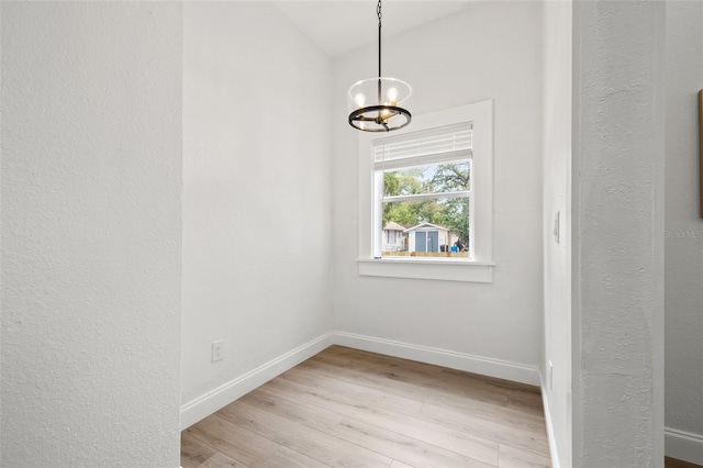 unfurnished dining area with baseboards, a notable chandelier, and light wood finished floors