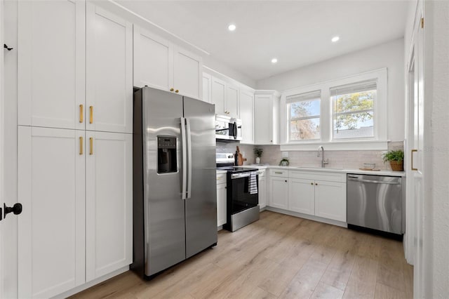 kitchen with a sink, stainless steel appliances, light wood-style floors, light countertops, and decorative backsplash