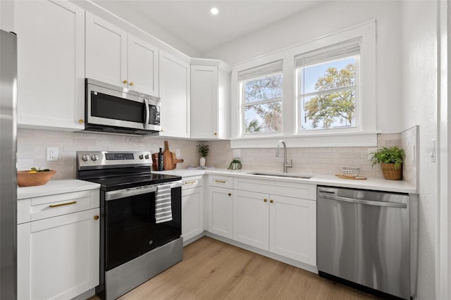 kitchen with light wood-style flooring, a sink, decorative backsplash, light countertops, and stainless steel appliances