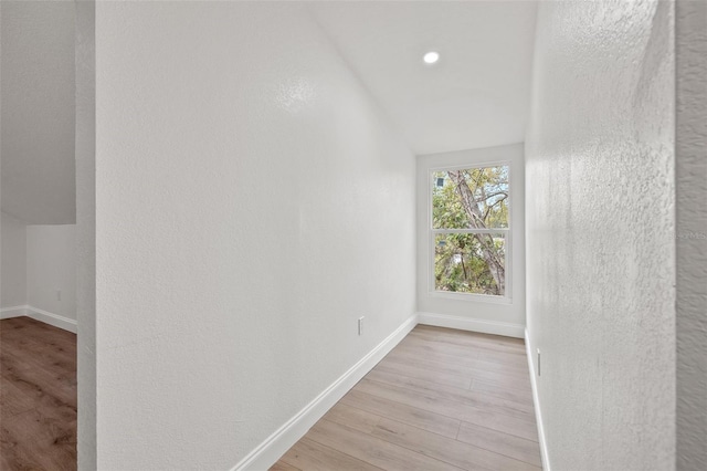 hall with baseboards, lofted ceiling, recessed lighting, light wood-style flooring, and a textured wall