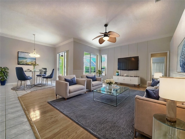 living area featuring a ceiling fan, a textured ceiling, wood finished floors, crown molding, and baseboards