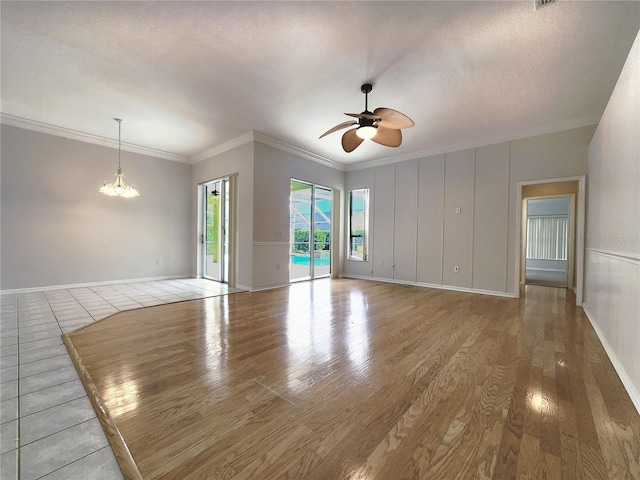 unfurnished living room with baseboards, ornamental molding, ceiling fan with notable chandelier, wood finished floors, and a textured ceiling