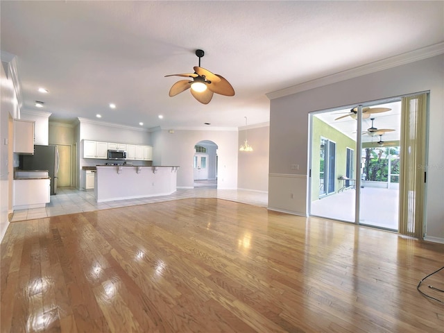 unfurnished living room featuring arched walkways, light wood-type flooring, a ceiling fan, and ornamental molding