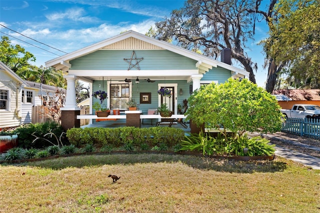 view of front facade with ceiling fan, fence, a front yard, covered porch, and a chimney