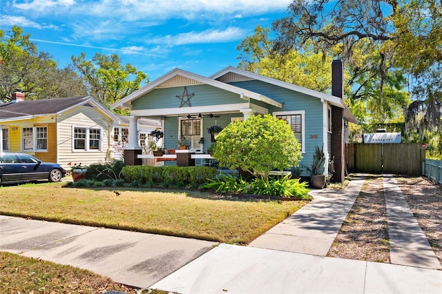 bungalow-style home with a front lawn, fence, a porch, a chimney, and a ceiling fan