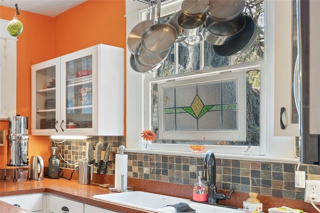 kitchen featuring white cabinets, glass insert cabinets, tasteful backsplash, and a sink