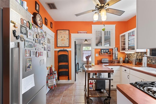 kitchen with visible vents, gas stovetop, stainless steel refrigerator, white cabinetry, and backsplash