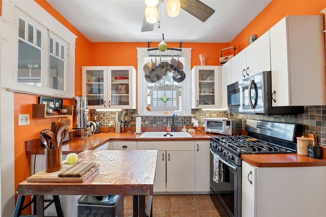 kitchen with a sink, stainless steel appliances, glass insert cabinets, white cabinetry, and backsplash