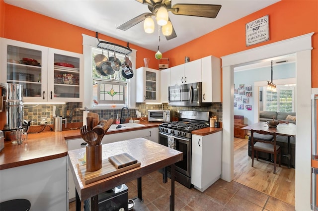 kitchen featuring a sink, backsplash, white cabinetry, stainless steel appliances, and glass insert cabinets