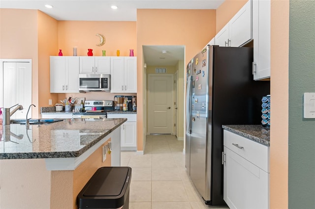 kitchen with light tile patterned floors, dark stone counters, a sink, stainless steel appliances, and white cabinetry