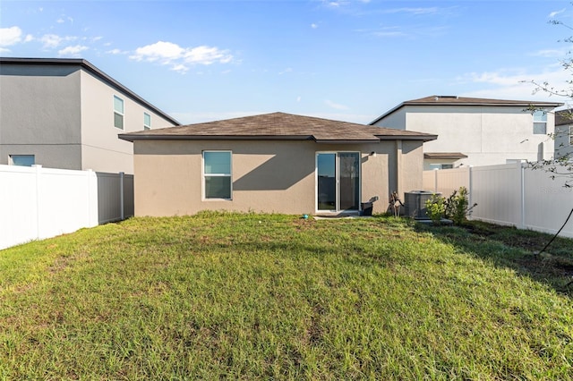 rear view of property featuring a yard, central AC unit, a fenced backyard, and stucco siding