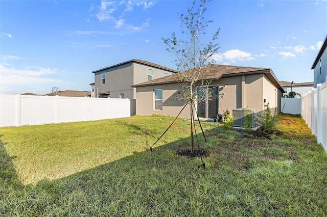 back of house with a yard, central AC unit, a fenced backyard, and stucco siding