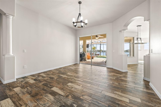 unfurnished dining area with decorative columns, baseboards, dark wood-style flooring, and ceiling fan with notable chandelier