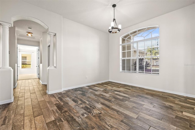 empty room featuring arched walkways, wood finished floors, baseboards, and decorative columns