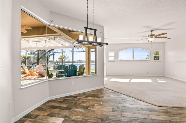 unfurnished dining area featuring a textured ceiling, baseboards, ceiling fan, and wood finished floors