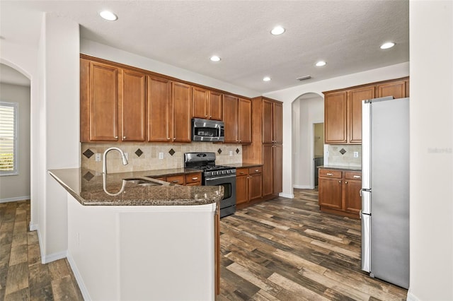 kitchen with a peninsula, arched walkways, appliances with stainless steel finishes, and a sink