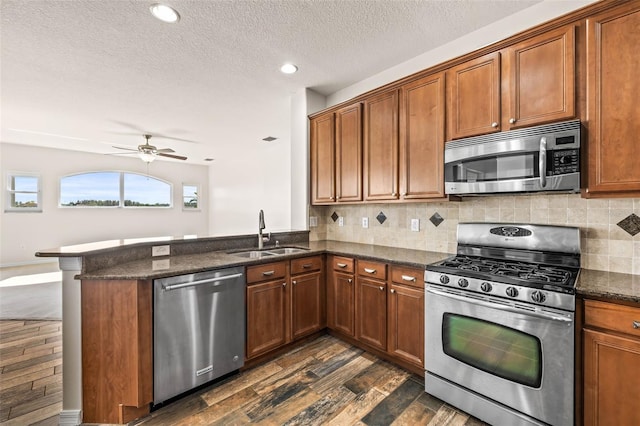 kitchen featuring a peninsula, a sink, dark wood-type flooring, appliances with stainless steel finishes, and brown cabinets