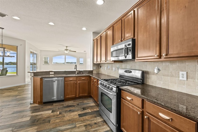 kitchen featuring brown cabinets, a sink, appliances with stainless steel finishes, a peninsula, and decorative backsplash