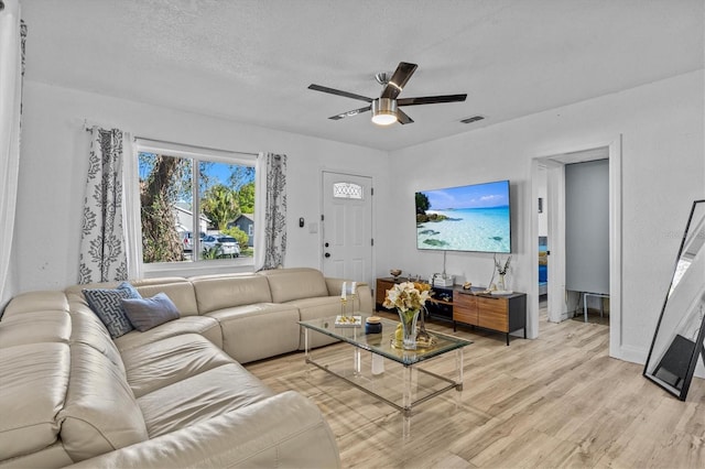 living room featuring light wood finished floors, visible vents, a textured ceiling, and a ceiling fan