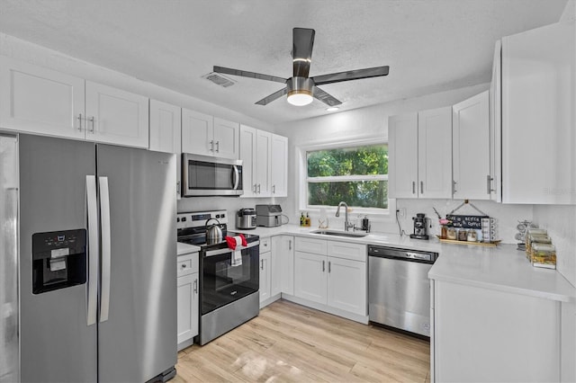 kitchen featuring a sink, white cabinetry, stainless steel appliances, light wood-style floors, and light countertops