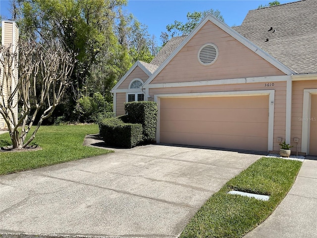 view of front of house featuring an attached garage, concrete driveway, a front yard, and a shingled roof