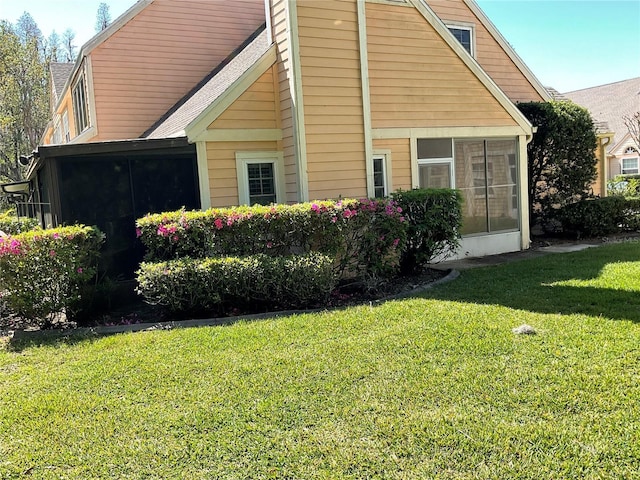 view of home's exterior featuring a lawn, a shingled roof, and a sunroom