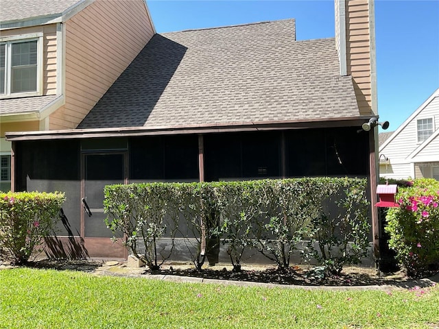 view of side of home featuring a sunroom, a lawn, roof with shingles, and a chimney