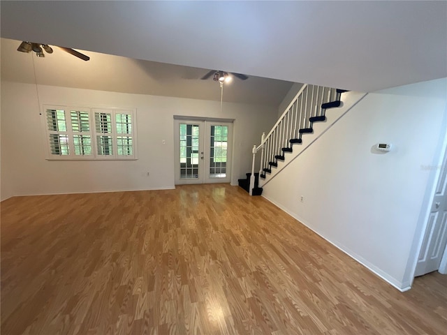 unfurnished living room with light wood finished floors, french doors, stairs, and ceiling fan