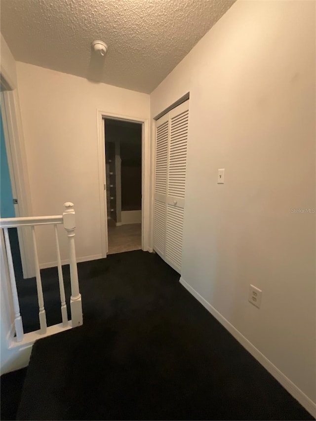 hall with an upstairs landing, baseboards, and a textured ceiling