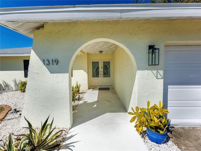 doorway to property featuring stucco siding, a garage, and french doors