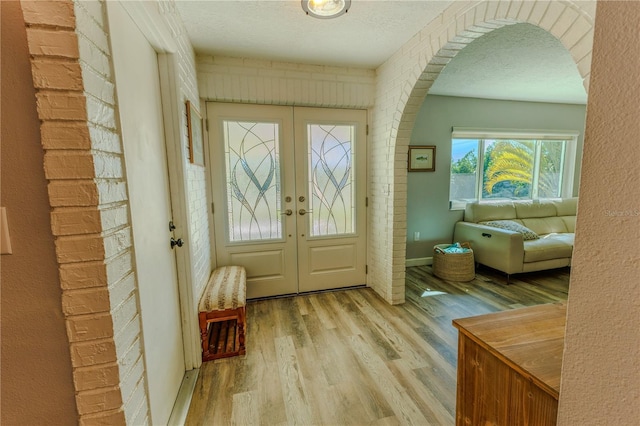 foyer entrance featuring a textured ceiling, french doors, arched walkways, brick wall, and light wood finished floors