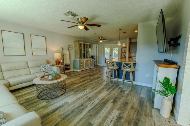 living room with visible vents, a textured ceiling, wood finished floors, french doors, and baseboards