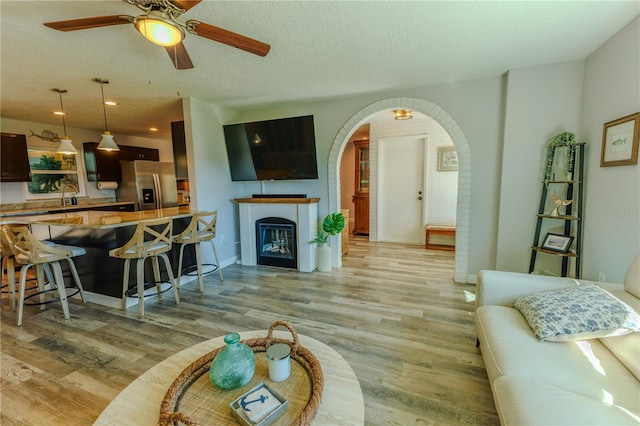 living area with a glass covered fireplace, light wood-style flooring, arched walkways, and a textured ceiling