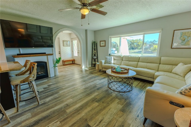 living room with a glass covered fireplace, wood finished floors, arched walkways, and a textured ceiling