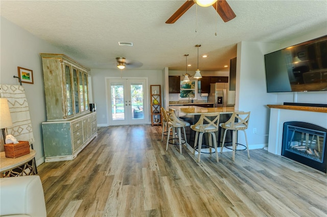 kitchen featuring a breakfast bar area, visible vents, french doors, stainless steel refrigerator with ice dispenser, and a glass covered fireplace