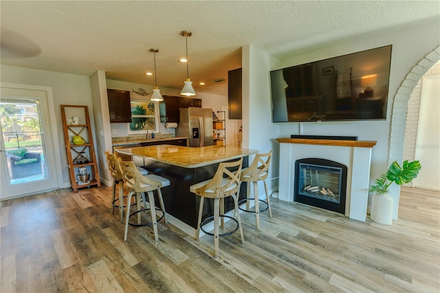 kitchen featuring light wood finished floors, stainless steel fridge, a kitchen breakfast bar, and light stone countertops