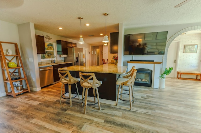 kitchen with a textured ceiling, a glass covered fireplace, stainless steel appliances, light wood-style floors, and a breakfast bar area