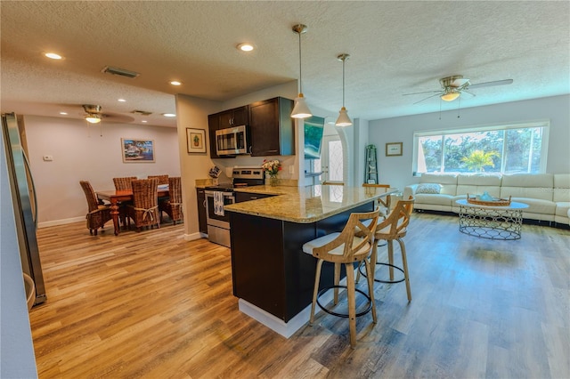 kitchen featuring open floor plan, a breakfast bar area, light stone counters, light wood-style floors, and stainless steel appliances