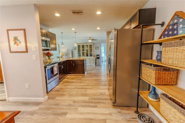 kitchen with visible vents, light wood finished floors, a peninsula, dark brown cabinetry, and appliances with stainless steel finishes