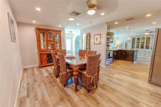 dining space with arched walkways, visible vents, light wood-style floors, and a ceiling fan