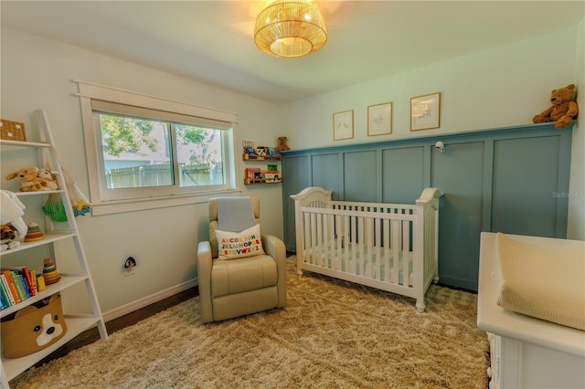 bedroom with a crib, a decorative wall, carpet floors, and wainscoting