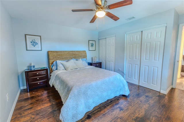 bedroom with a ceiling fan, visible vents, baseboards, dark wood finished floors, and multiple closets