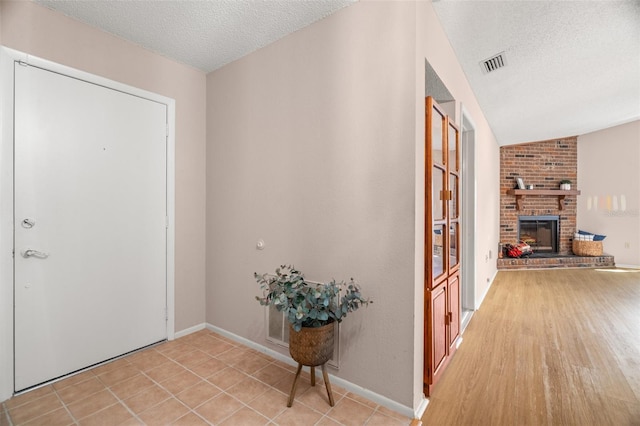 foyer entrance with visible vents, a brick fireplace, baseboards, light tile patterned floors, and a textured ceiling