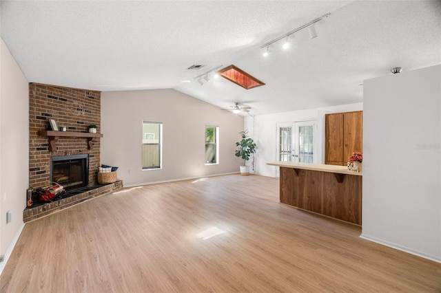 unfurnished living room with visible vents, a textured ceiling, baseboards, light wood finished floors, and lofted ceiling