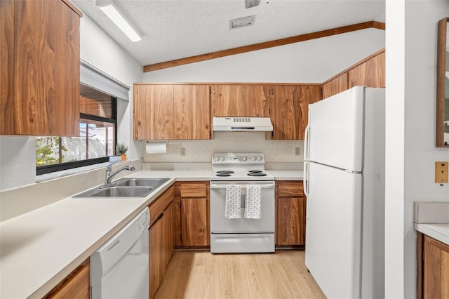 kitchen with under cabinet range hood, lofted ceiling, brown cabinetry, white appliances, and a sink