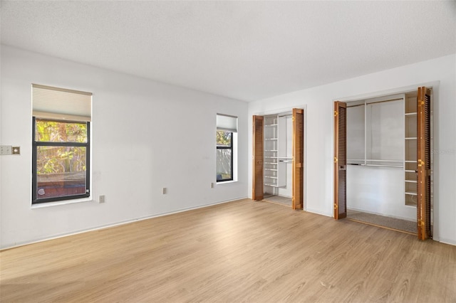 unfurnished bedroom featuring multiple windows, multiple closets, light wood finished floors, and a textured ceiling