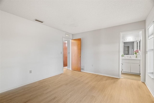 unfurnished room featuring visible vents, baseboards, a textured ceiling, and light wood finished floors