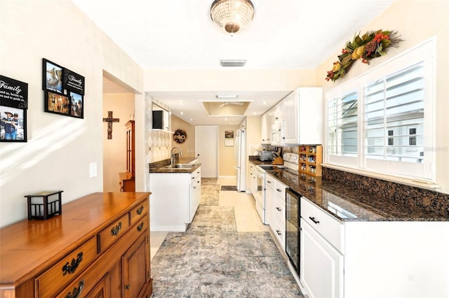 kitchen with visible vents, beverage cooler, white appliances, white cabinetry, and a sink