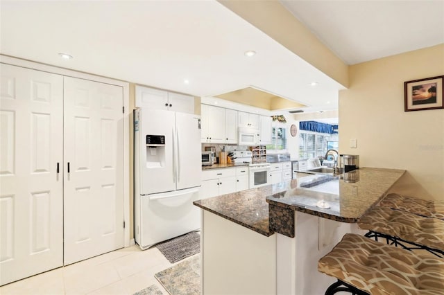 kitchen with a kitchen breakfast bar, a peninsula, white appliances, white cabinetry, and a sink